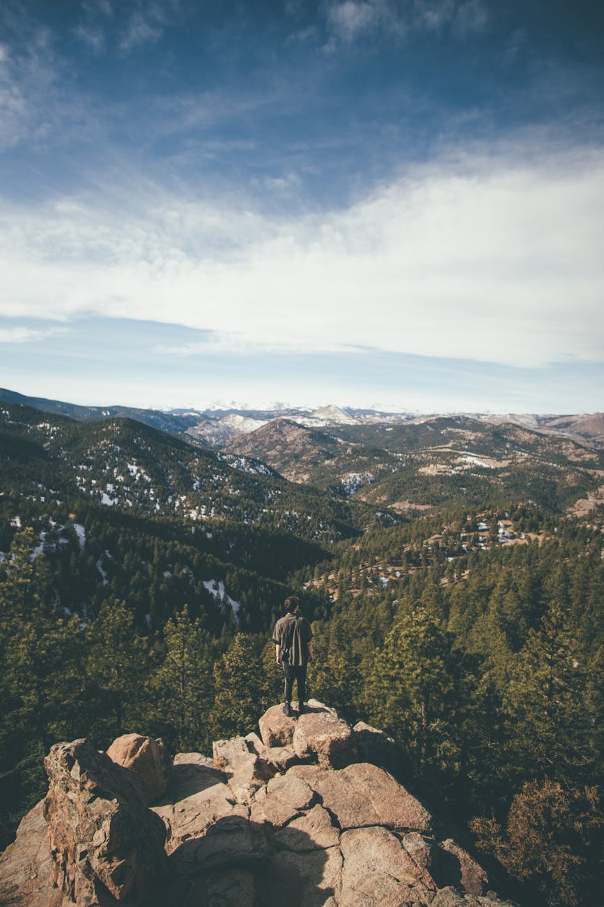 photo of man standing on cliff edge across mountains